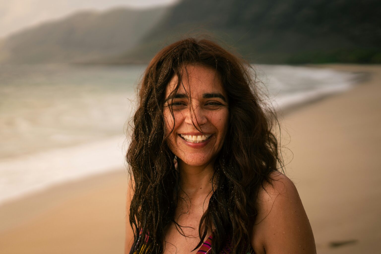 Joyful woman with windswept hair enjoying sunset on a scenic beach.